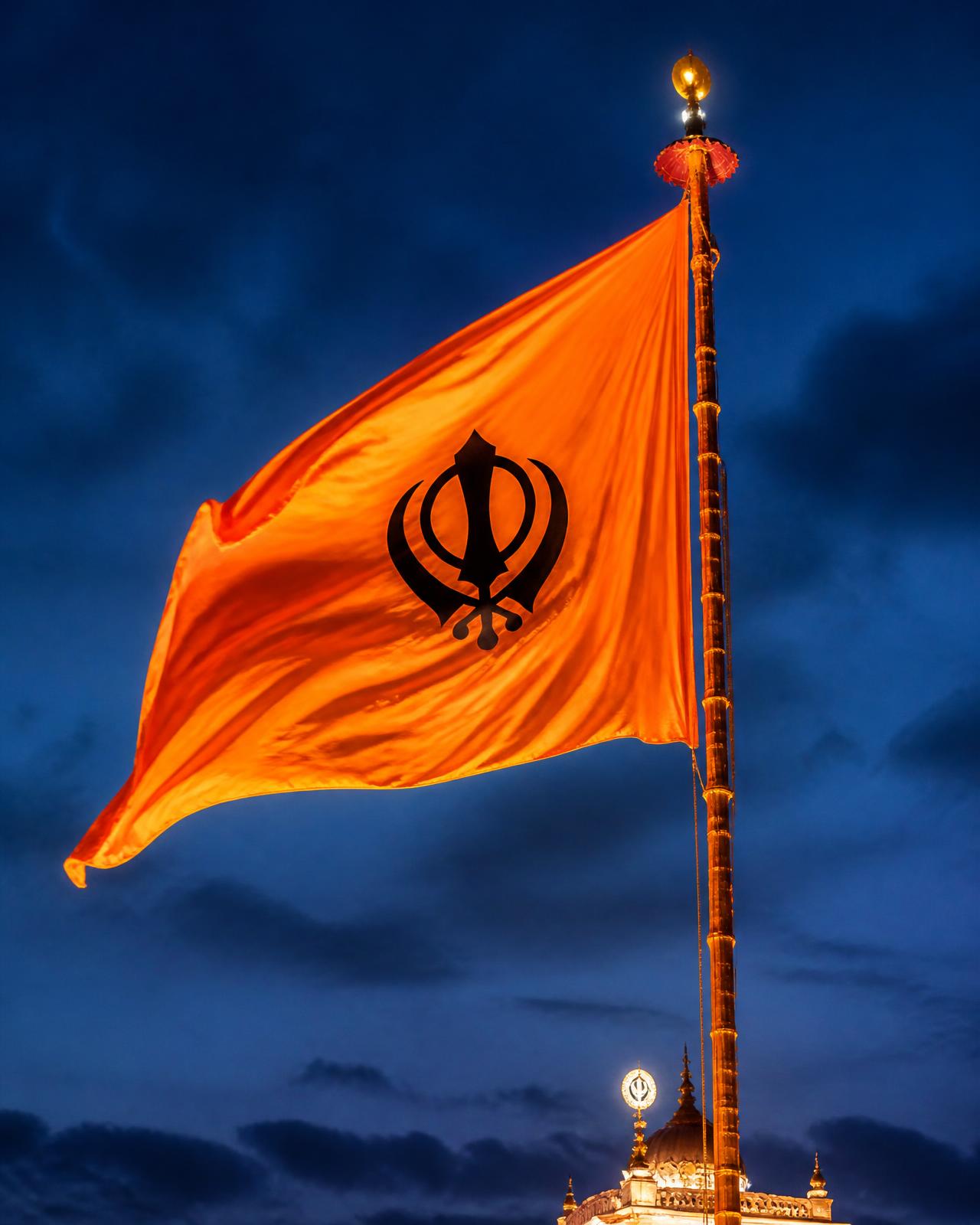 A saffron Nishan Sahib flag rising against a deep blue sky at golden light
